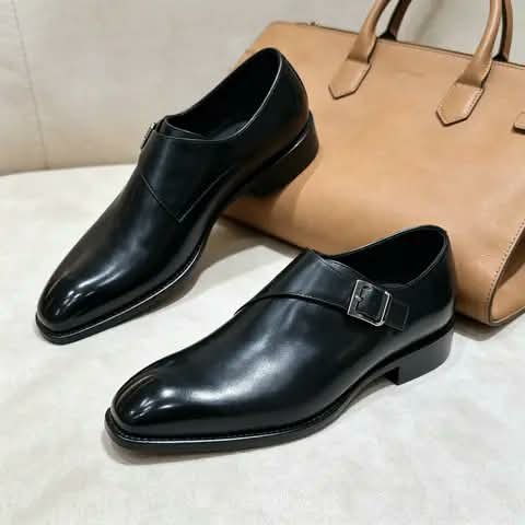 Black monk strap shoes beside a tan bag.