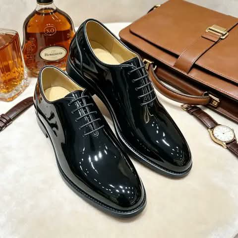 Black patent Oxford shoes beside a briefcase and a watch.