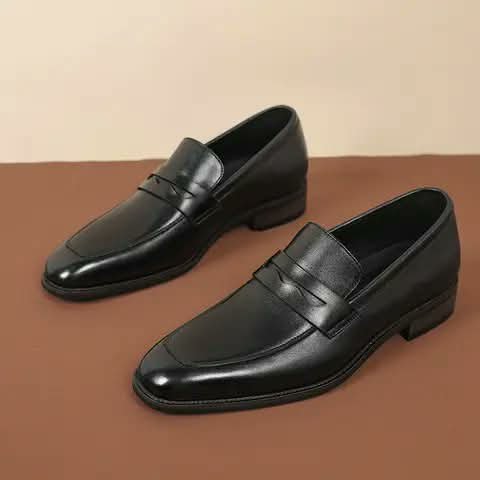 Black penny loafers on a brown surface.