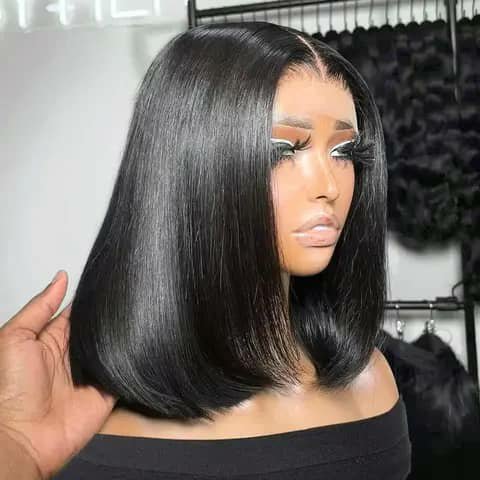 A straight black bob wig on a mannequin head, a hand holding the side.