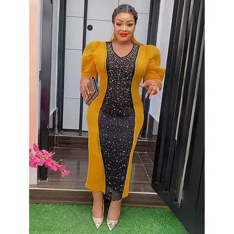 A woman wearing a long fitted dress with a black sequinned centre panel and mustard-yellow sides and puffed sleeves, holding a clutch, outdoors.
