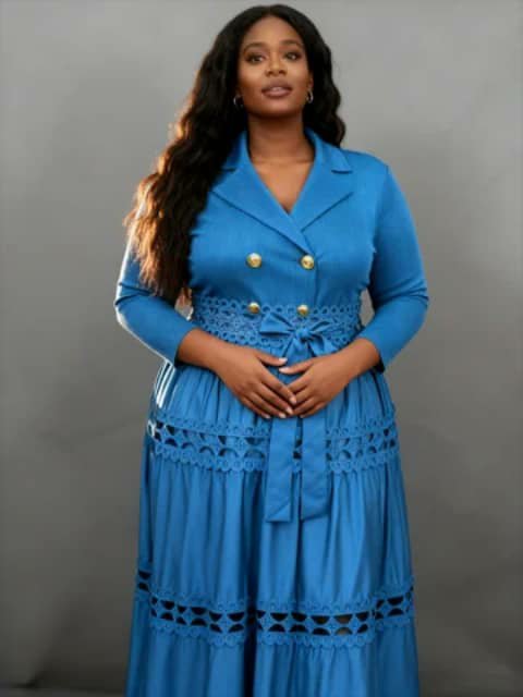 A woman wearing a long blue shirt-style dress with gold buttons, a lace waist tie and a tiered lace-trim skirt.