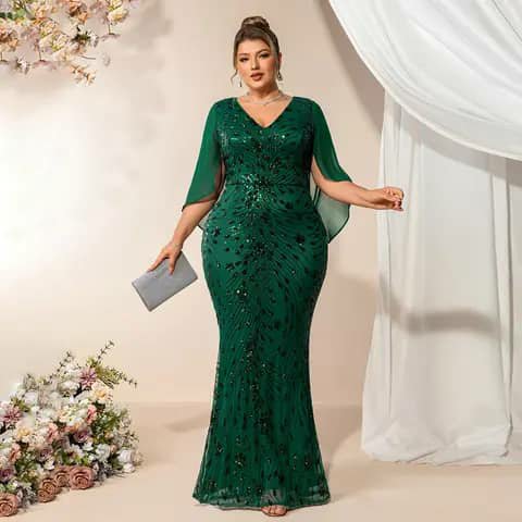 A woman wearing a long dark-green sequinned fitted dress with cape sleeves, holding a clutch.