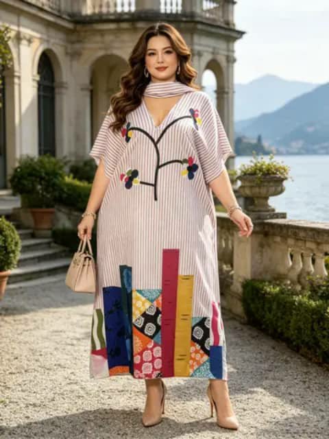 A woman wearing a long loose striped dress with a floral branch print and a colourful patchwork hem, holding a bag, outdoors.
