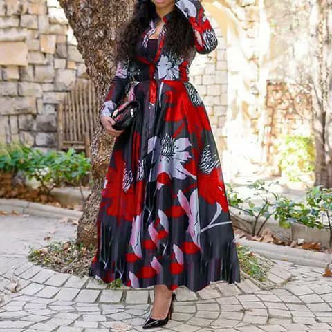 A woman wearing a long red, black and white floral print dress with long sleeves, holding a clutch, outdoors.