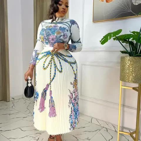 A woman wearing a white pleated dress with a floral print and a tassel belt.