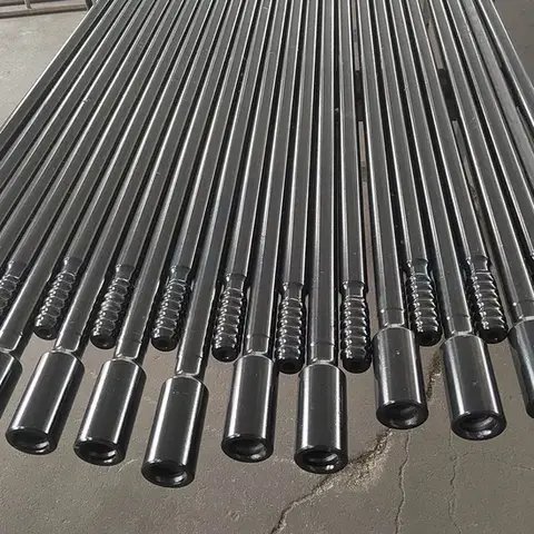 A long row of black drill rods lying on the ground.