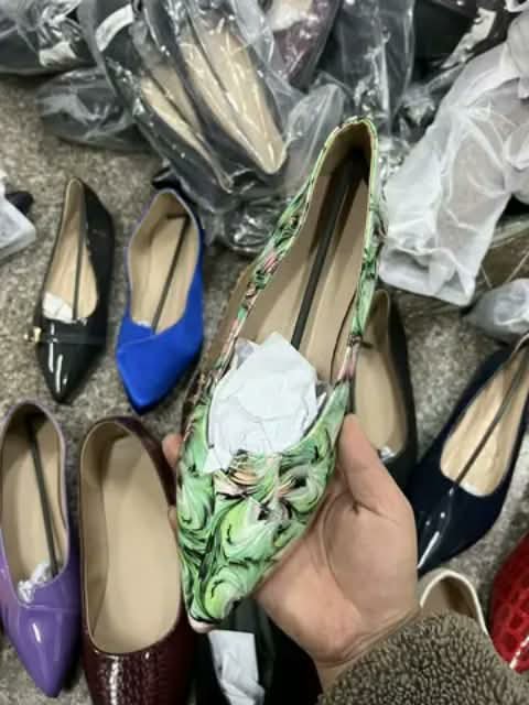 A green floral flat shoe held in hand, more flats around it.