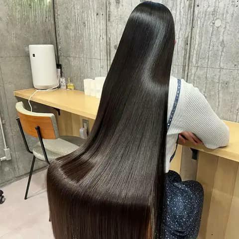 A seated woman with extremely long straight dark-brown hair reaching past her waist, seen from behind.