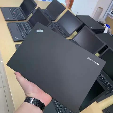Black Lenovo ThinkPad lid held up over a desk of laptops