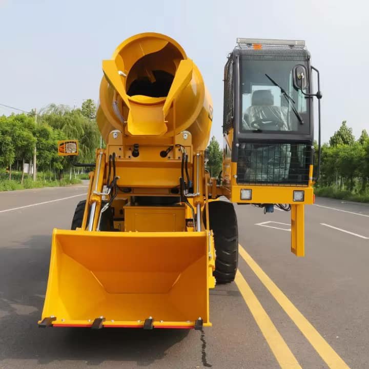 A yellow self-loading concrete mixer seen from the front, parked on a road.