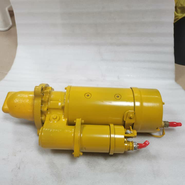 A yellow starter motor with red terminals, lying on white cloth.