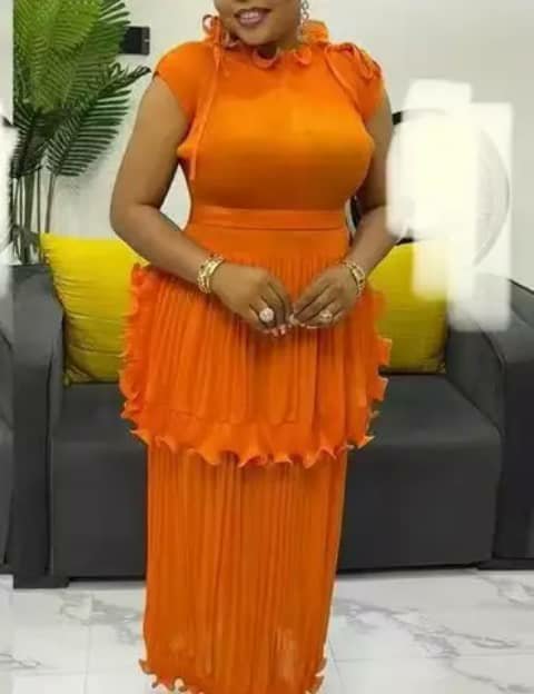 A woman wearing an orange two-piece set with a ruffled top and a pleated skirt, indoors.